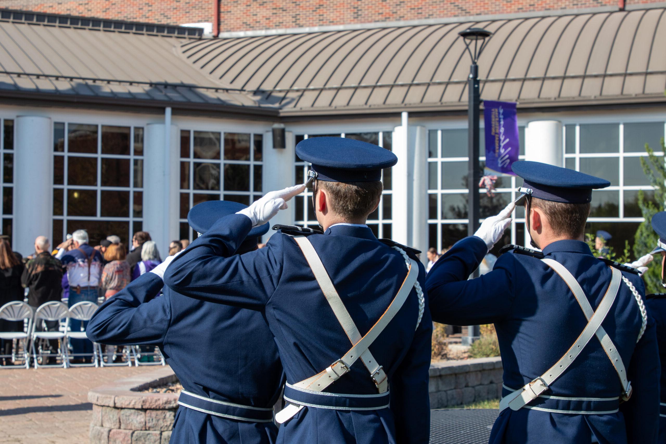 Two people in uniform saluting flag