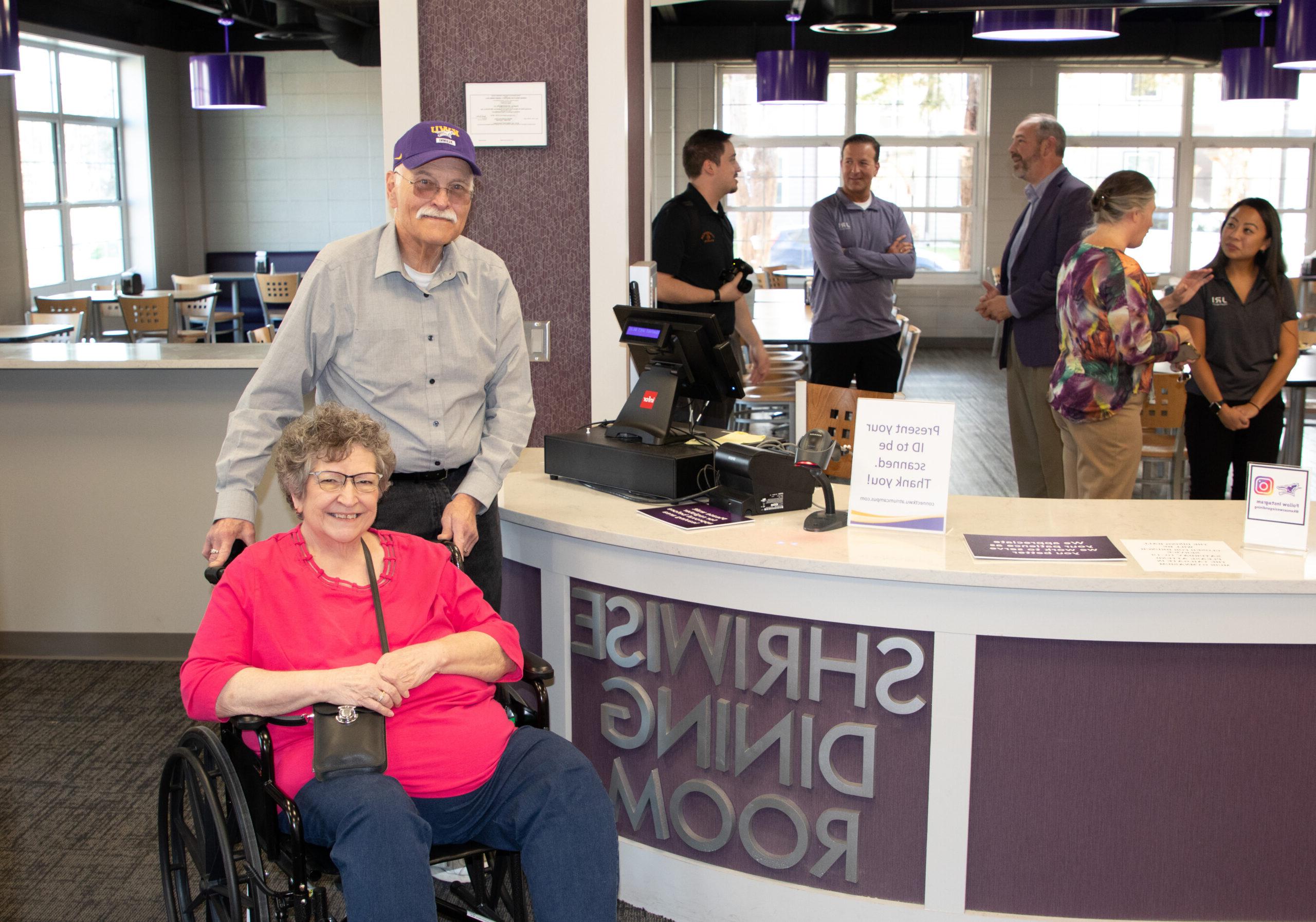 Man and woman in wheelchair next to dining room sign